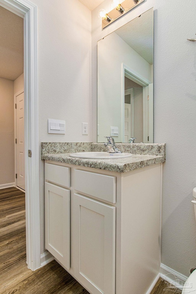 half bath featuring toilet, wood finished floors, vanity, and baseboards