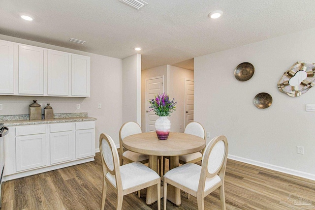dining space featuring a textured ceiling, visible vents, wood finished floors, and baseboards