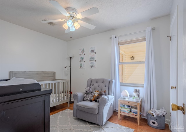 bedroom with a nursery area, a textured ceiling, and light hardwood / wood-style flooring