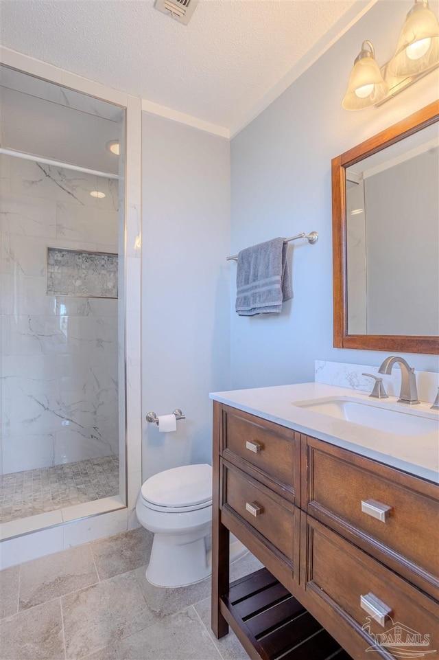 bathroom with a tile shower, vanity, a textured ceiling, and toilet