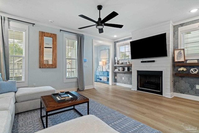 living area featuring ceiling fan, a fireplace, baseboards, and wood finished floors