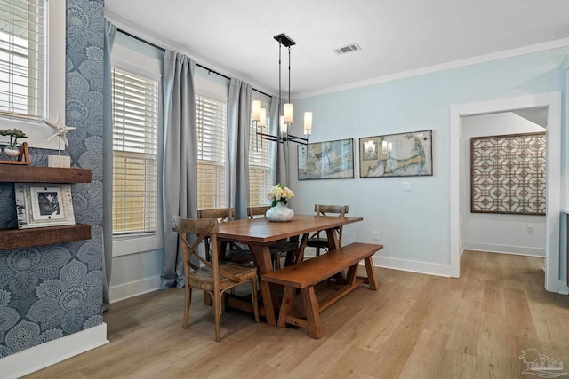 dining room featuring crown molding, light wood-type flooring, visible vents, and an inviting chandelier