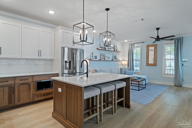 kitchen featuring black microwave, light wood finished floors, stainless steel refrigerator with ice dispenser, and backsplash