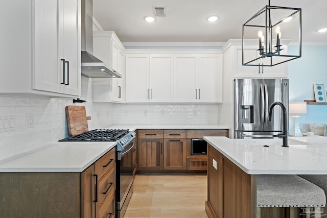 kitchen with visible vents, light wood-style flooring, stainless steel appliances, wall chimney range hood, and white cabinetry