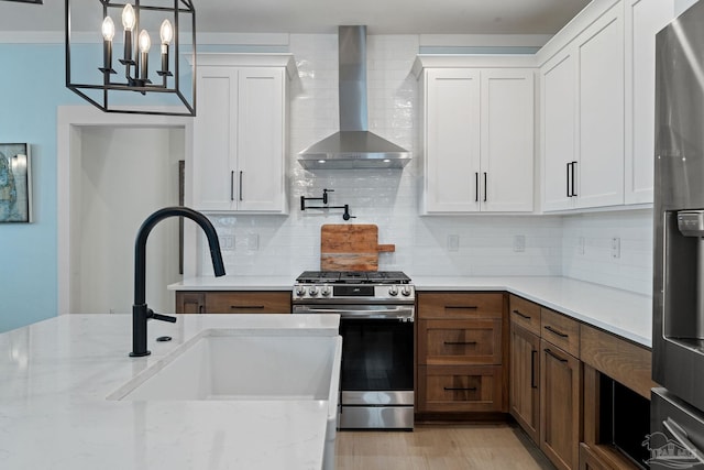 kitchen with tasteful backsplash, stainless steel appliances, wall chimney range hood, white cabinetry, and a sink