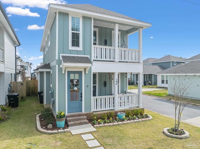 view of front facade featuring board and batten siding, a front yard, covered porch, and a balcony