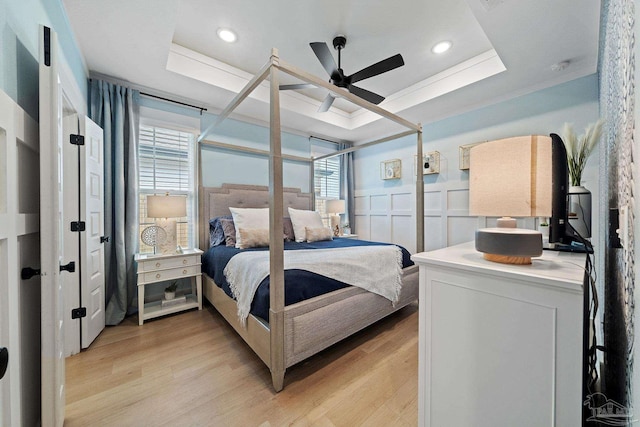 bedroom featuring light wood-type flooring, a tray ceiling, wainscoting, and a decorative wall