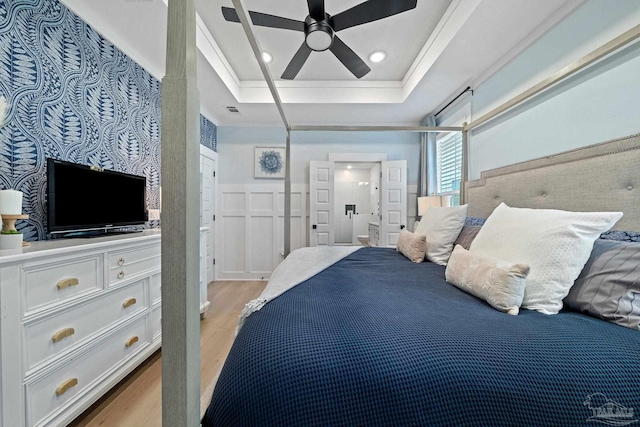 bedroom featuring light wood finished floors, a raised ceiling, a wainscoted wall, a decorative wall, and recessed lighting