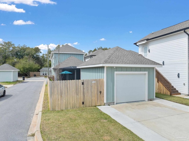 exterior space with roof with shingles, a yard, concrete driveway, fence, and a garage