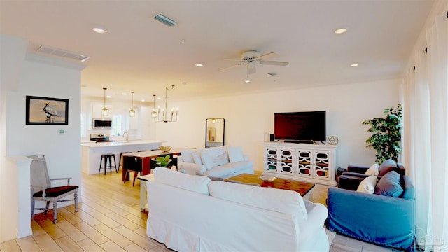 living room featuring ceiling fan with notable chandelier, crown molding, light hardwood / wood-style flooring, and sink