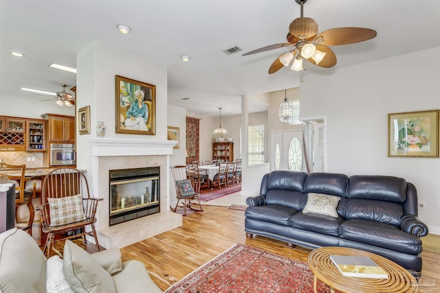 living room featuring a tile fireplace, light hardwood / wood-style flooring, and ceiling fan with notable chandelier