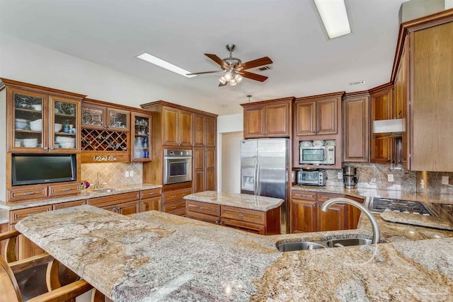 kitchen featuring light stone countertops, sink, stainless steel appliances, decorative backsplash, and a breakfast bar