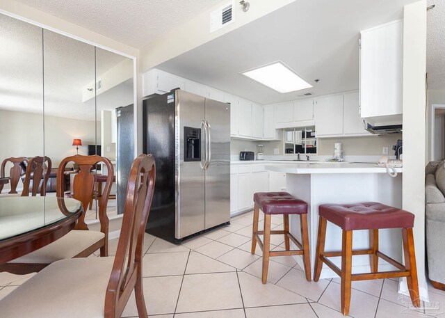 kitchen featuring visible vents, white cabinets, stainless steel fridge, light countertops, and a peninsula