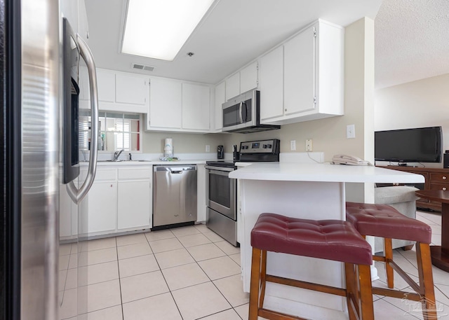 kitchen featuring a peninsula, light tile patterned floors, light countertops, appliances with stainless steel finishes, and a sink