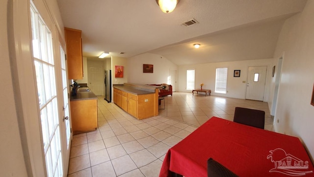 kitchen with light tile patterned floors, vaulted ceiling, and stainless steel fridge