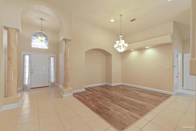 tiled entryway featuring decorative columns, a towering ceiling, and a notable chandelier