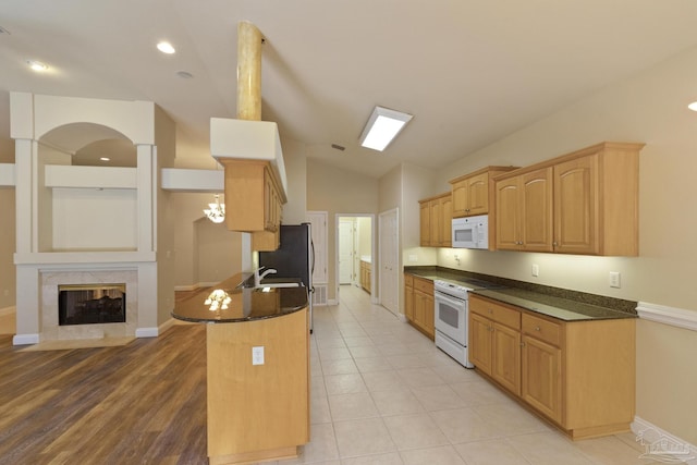 kitchen featuring white appliances, dark stone counters, sink, vaulted ceiling, and a premium fireplace