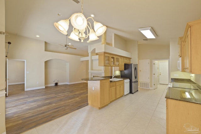 kitchen featuring kitchen peninsula, white appliances, ceiling fan with notable chandelier, pendant lighting, and a high ceiling