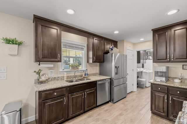 kitchen with dark brown cabinets, appliances with stainless steel finishes, light wood-style floors, and a sink