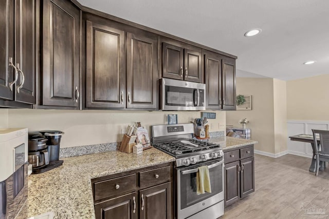 kitchen with dark brown cabinets, stainless steel appliances, light wood-style floors, and light stone countertops