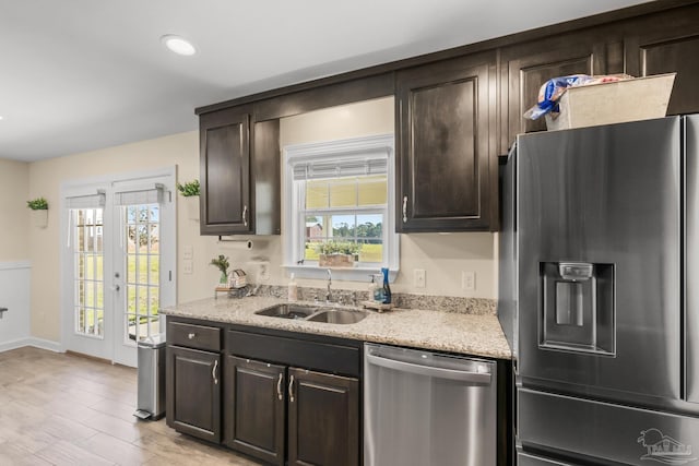 kitchen with light stone countertops, dark brown cabinetry, light wood-style floors, stainless steel appliances, and a sink