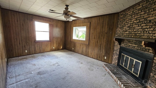 unfurnished living room with light colored carpet, a brick fireplace, ceiling fan, and wooden walls