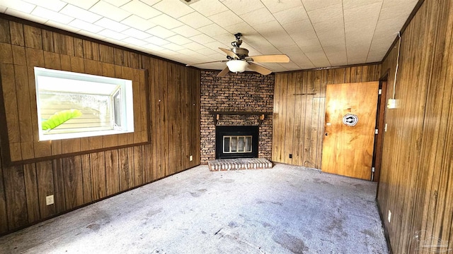 unfurnished living room with carpet, ceiling fan, a fireplace, and wooden walls