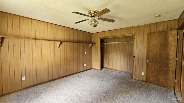 unfurnished bedroom with ceiling fan, wood walls, a textured ceiling, light carpet, and a closet