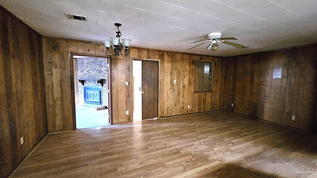 empty room featuring ceiling fan with notable chandelier, wood walls, and wood-type flooring