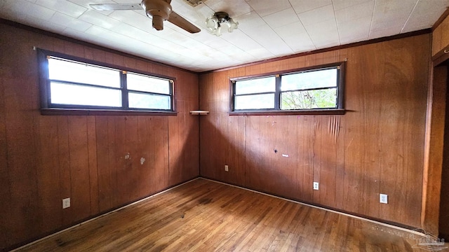 empty room with wooden walls, a healthy amount of sunlight, and hardwood / wood-style flooring