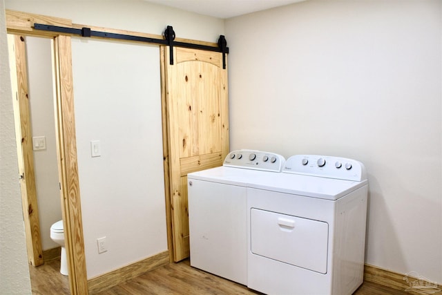 washroom featuring a barn door, washing machine and dryer, laundry area, baseboards, and light wood finished floors