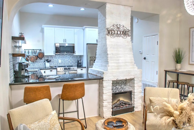 kitchen featuring white cabinets, appliances with stainless steel finishes, light hardwood / wood-style floors, kitchen peninsula, and a kitchen breakfast bar