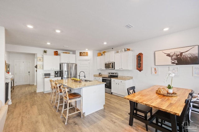 kitchen with a breakfast bar area, appliances with stainless steel finishes, light stone countertops, white cabinets, and a center island with sink