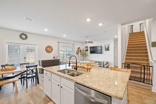 kitchen featuring dishwasher, sink, white cabinets, light stone countertops, and a center island with sink