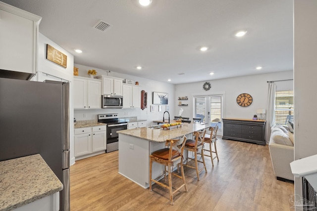 kitchen featuring sink, a breakfast bar area, appliances with stainless steel finishes, light stone countertops, and white cabinets