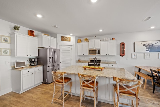 kitchen with stainless steel appliances, white cabinetry, a breakfast bar, and sink