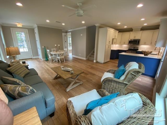 living room with ornamental molding, sink, light hardwood / wood-style flooring, and ceiling fan