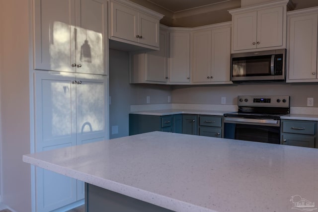 kitchen with gray cabinets, crown molding, light stone countertops, and stainless steel appliances