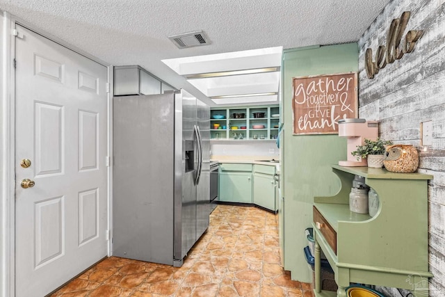 kitchen featuring stainless steel fridge, a textured ceiling, and green cabinets