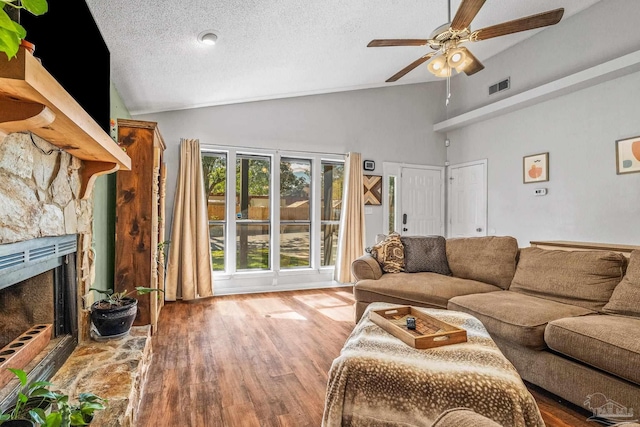 living room with lofted ceiling, a stone fireplace, a textured ceiling, ceiling fan, and hardwood / wood-style floors