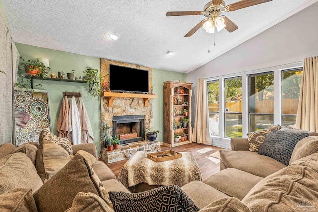 living room with a stone fireplace, vaulted ceiling, a textured ceiling, ceiling fan, and light hardwood / wood-style floors