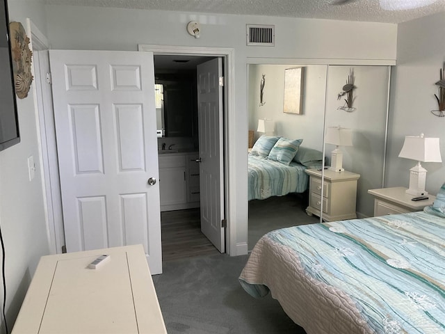 bedroom with ensuite bath, dark carpet, a textured ceiling, sink, and a closet