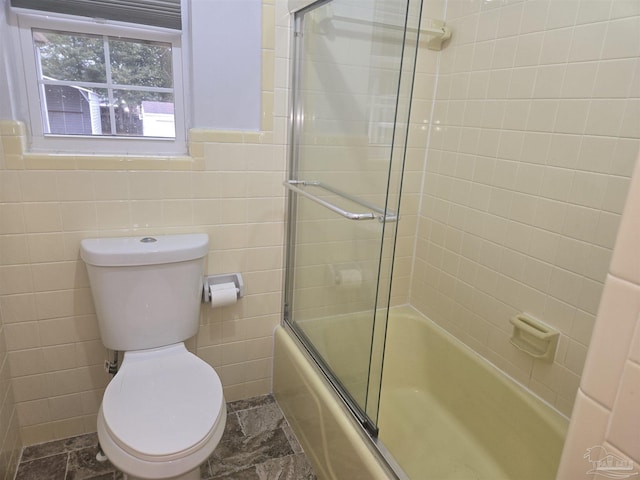 bathroom featuring toilet, shower / bath combination with glass door, and tile walls