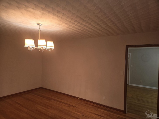 spare room featuring a chandelier and dark wood-type flooring