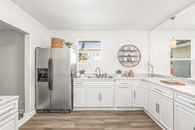 kitchen with stainless steel refrigerator with ice dispenser, light wood-type flooring, sink, decorative light fixtures, and white cabinets