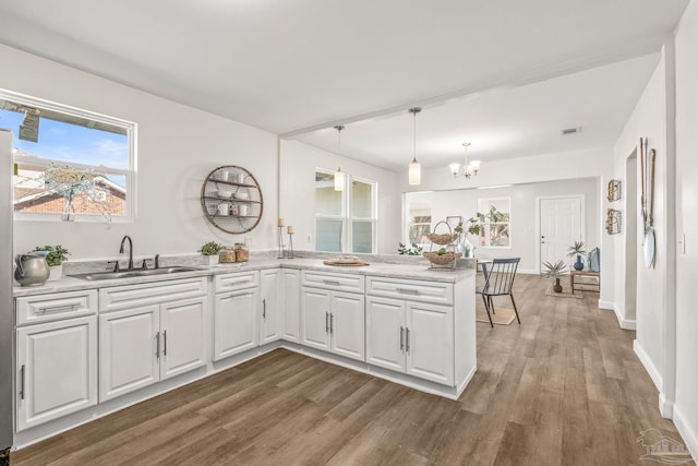 kitchen featuring kitchen peninsula, sink, wood-type flooring, a notable chandelier, and white cabinets