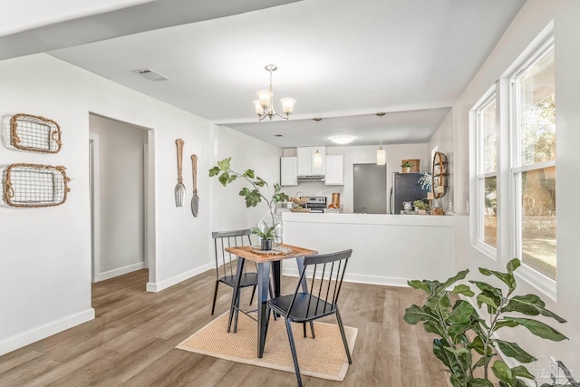 dining room with a wealth of natural light, light hardwood / wood-style flooring, and an inviting chandelier