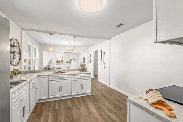 kitchen featuring pendant lighting, kitchen peninsula, hardwood / wood-style flooring, white cabinetry, and a chandelier