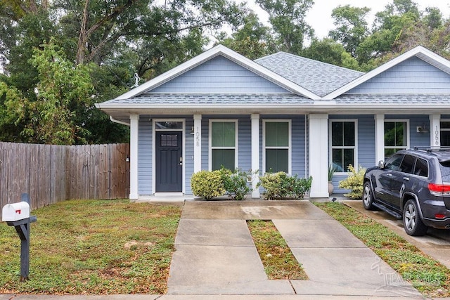 view of front of home with roof with shingles, a porch, and fence