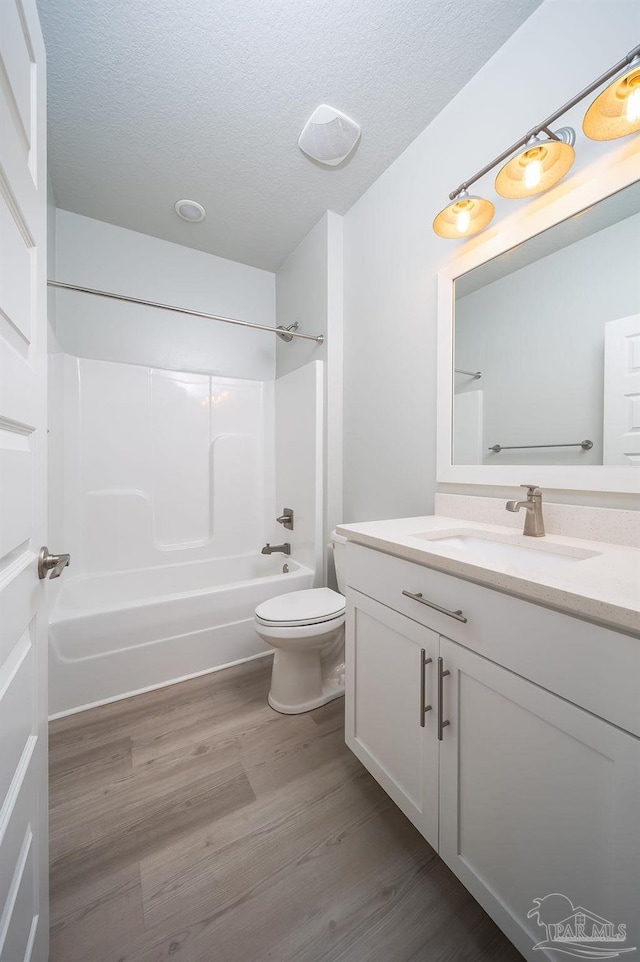 full bathroom with a textured ceiling, wood-type flooring, vanity, shower / washtub combination, and toilet